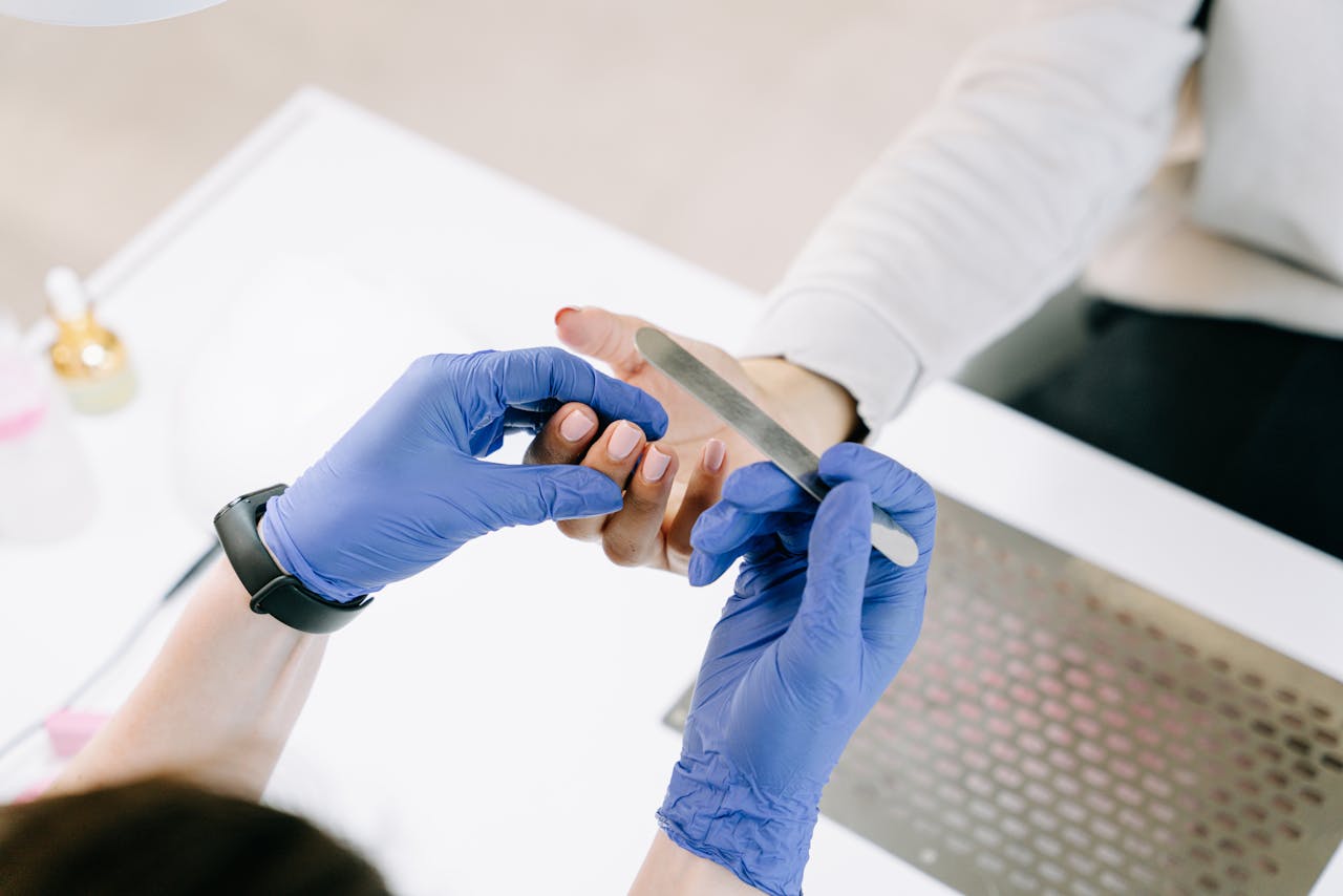 Close-up of a nail technician filing a clients nails with blue gloves in a professional setting.
